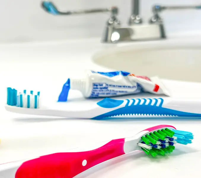 Two toothbrushes stting next to a small tube of toothpaste on a sink 